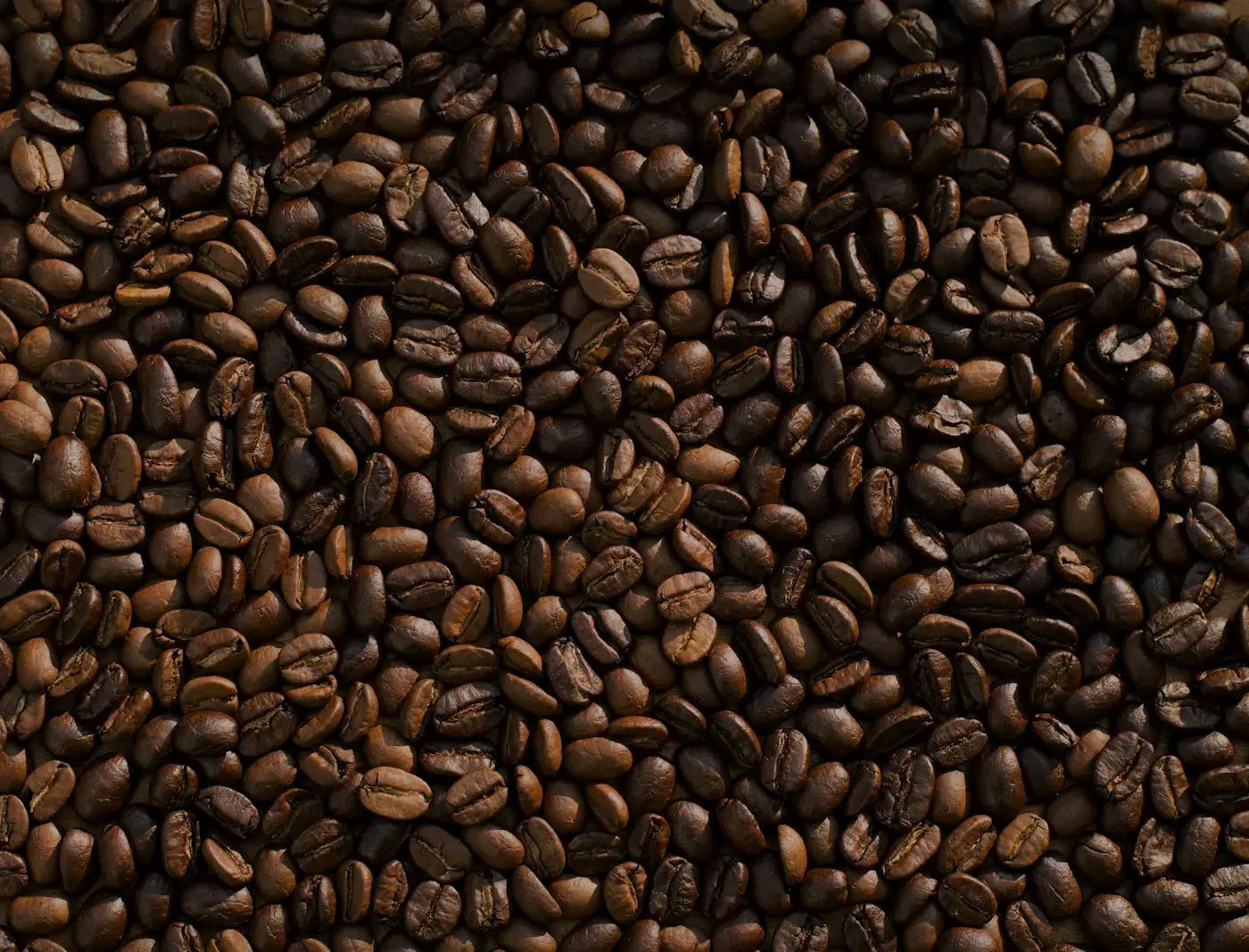 Roasted coffee beans spread across a dark surface