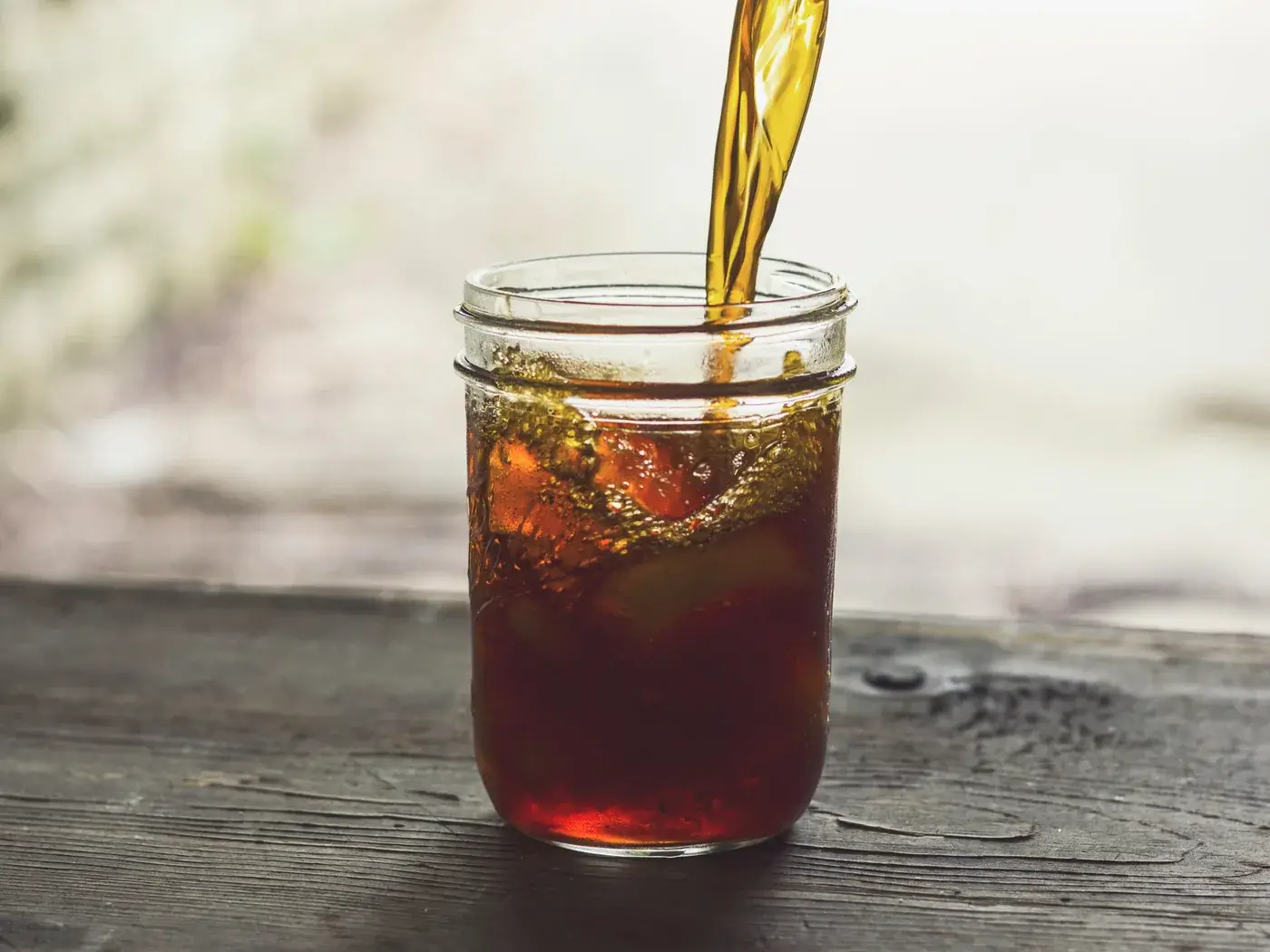 Cold brew poured over ice into a glass jar on a wooden ledge