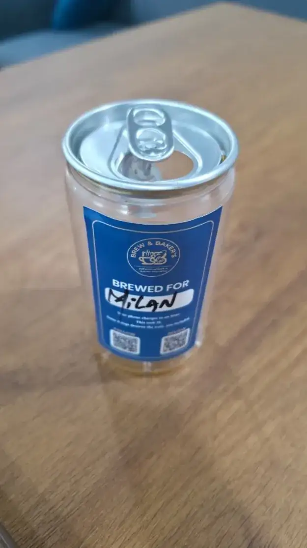 A clear Brew & Baker's can with a pull-tab lid, its blue label reading "Brewed for Milan" in handwriting